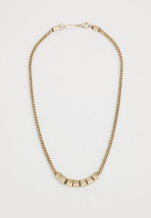 Gold metal chain necklace featuring a woven design and lettered blocks spelling "LACOSTE." Clasp closure with smooth accents.