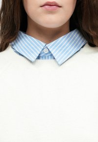 White knit sweater over a light blue striped shirt, featuring a button-down collar. The shirt has two buttons visible at the collar.