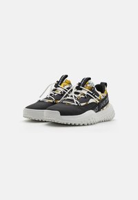 Des baskets noires et jaunes présentent une semelle en caoutchouc texturé, un bout renforcé et de larges lacets blancs. Des accents à motifs rehaussent le design.