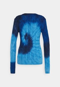Blå kabelstickad tröja med lång ärm som har ett mörkblått tie-dye spiralmönster på baksidan.