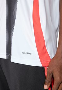 AEROREADY athletic shirt featuring white base, black diagonal stripes, and red side accents. Soft, moisture-wicking fabric, short sleeves.