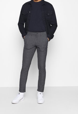 Grey checkered trousers with a slim fit, paired with a navy t-shirt and a black jacket. Finished with white sneakers.