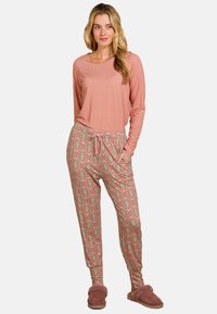 Lange mouwen roze top met een gestructureerd patroon, gecombineerd met een broek met koord in een patroon met bloemen in roze en groen, en zachte slippers.