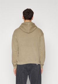 Felpa con cappuccio color khaki a vestibilità rilassata, con polsini e orlo a costine, texture morbida e dettagli minimi sul retro.