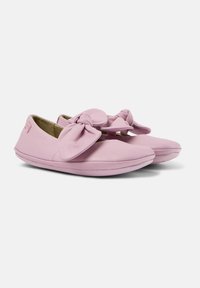 Zapatos de piel rosa claro tipo slip-on que cuentan con un gran lazo en la parte frontal, puntera redondeada y suela de goma flexible. Textura suave y diseño sencillo.