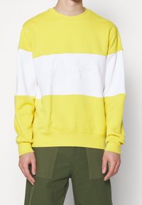 Gul och vit sweatshirt med rund halsringning, med en stor präglad Nike-logga över bröstet och ribbade muddar och nederkant.