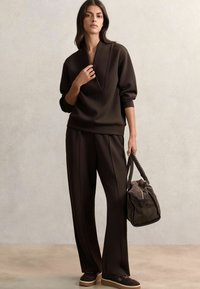 Sudadera marrón con un profundo escote en V y mangas holgadas, combinada con pantalones de pierna ancha a juego. En una mano se sostiene un bolso marrón texturizado.