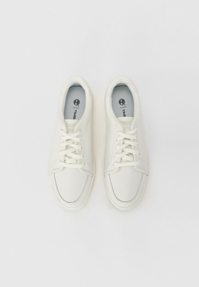 Zapatillas de cuero blancas con punta redonda, diseño de cordones y forro interior gris en contraste. Presentan un logo en la plantilla y suela texturizada.