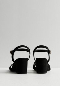 Svarta mocka blockklacksandaler med ankelremmar, utrustade med ett justerbart spänne och minimala dekorativa detaljer.