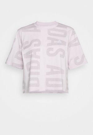 T-shirt court Adidas rose clair avec grand texte vertical estompé et manches courtes sur fond blanc.