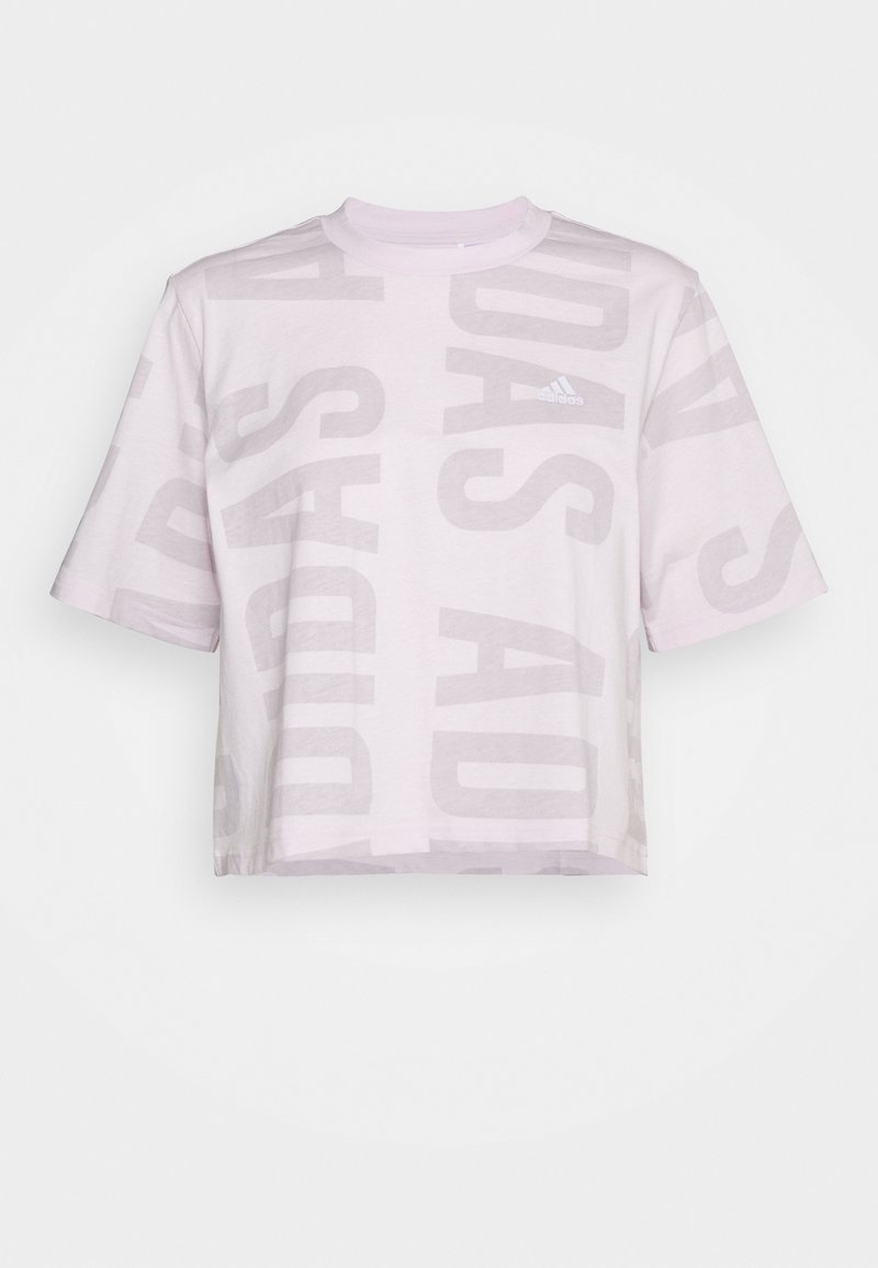 T-shirt court Adidas rose clair avec grand texte vertical estompé et manches courtes sur fond blanc.