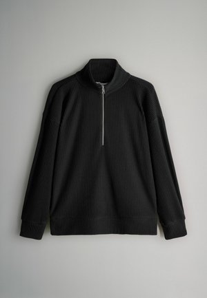 Must mustriba pikkade varrukatega pullover, kõrge kraega ja ees poole lukuga, lamab helesinise tausta vastu.