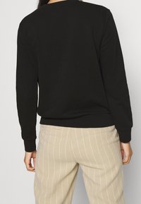 Jersey negro de manga larga con dobladillo acanalado, combinado con pantalones a rayas beige. La tela parece suave y tiene una textura lisa.