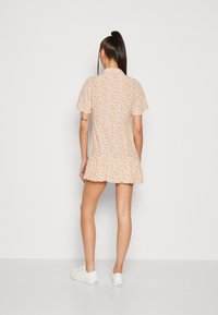 Robe imprimée fleurie en orange pâle avec des manches courtes, un ourlet évasé et un col à revers. Associée à des baskets blanches.