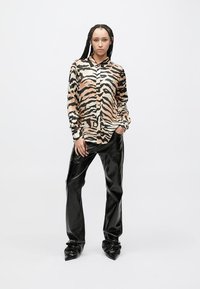 Loomamustriga särk beeži ja musta värviga, nööpidega ees. Mustrile lisanduvad läikivad mustad lehvikpüksid ja teravate, voltidega kontsakingad.