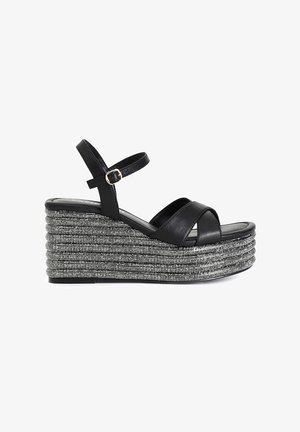 Sandalias de cuña de cuero negro con tiras entrecruzadas, que presentan un diseño de cuerda plateada en la plataforma y una hebilla en la correa del tobillo.