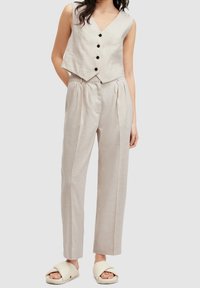 Ljust beige lin väst med V-ringning och svarta knappar, ihop med matchande plisserade byxor och krämfärgade sandaler. Slen yta, skräddarsydd passform.
