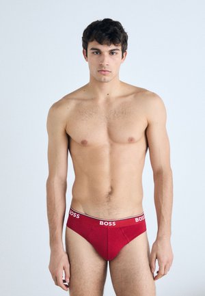 Rote Baumwollslips mit einem elastischen Bund in Weiß und Schwarz, der das "BOSS"-Logo trägt. Glatte Textur, enganliegende Passform, klassisches Design.