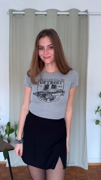 Pilkas marškinėliai su užrašu „MOTOR CLUB DETROIT“ ir juoda mini sijonas su šonine skeltuku. Komplektą užbaigia permatomos juodos pėdkelnės.