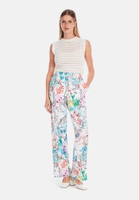 Weißes gestricktes ärmelloses Oberteil, kombiniert mit weitem Hosenbeinen, die ein farbenfrohes Blumenmuster aufweisen, akzentuiert mit grünen, pinken und blauen Details.