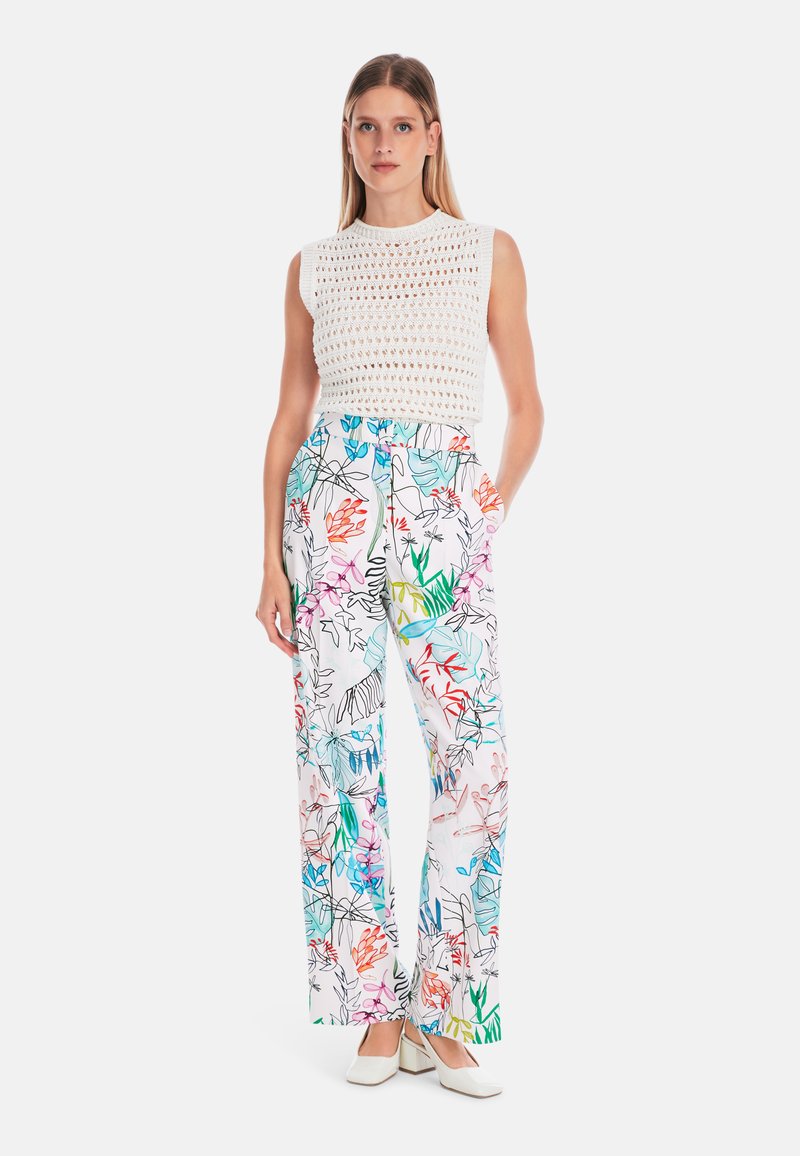 Weißes gestricktes ärmelloses Oberteil, kombiniert mit weitem Hosenbeinen, die ein farbenfrohes Blumenmuster aufweisen, akzentuiert mit grünen, pinken und blauen Details.