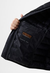 Sort isoleret jakke med quiltet tekstur, der har et logo patch og en lynlås indvendig lomme, holdt åben for at vise interiøret.