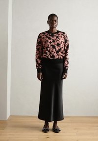 Ženska pletena črna pulover z cvetličnim vzorcem in rožami v roza barvi, v kombinaciji s prilegajočo črno krilom in črnimi balerinkami z dekorativnim okrasjem.