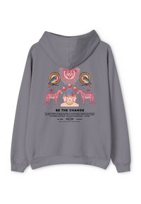 Sudadera gris con un estampado gráfico colorido de leones, cebras y aves, junto con el texto "SÉ EL CAMBIO" en negrita.