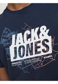 Camiseta de algodón azul marino con gran texto blanco "JACK & JONES." Gráfico de un mapa de la ciudad en azul y rosa claro, con texto debajo para la marca.