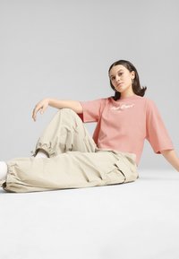 Rúžová oversized tričko s bielou výšivkou, skombinované s voľnými béžovými cargo nohavicami. Hladká látka, uvoľnený strih a elastické manžety na nohaviciach.