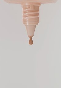 Lichtbeige knijpflesdop met een glad, crèmig druppeltje dat aan de tuit hangt, tegen een witte achtergrond.