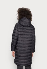 Zwarte donzen jas met horizontale stiksels, een capuchon en lange mouwen. Gladde textuur en halflang tot op de dijen, ontworpen voor warmte.