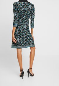 Czarna sukienka z rękawami do trzech ćwiartek, zdobiona wielokolorowym okrągłym wzorem i paskiem u dołu. W komplecie z czarnymi sandałami na wysokim obcasie.