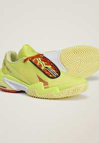 Felgele sportschoenen met rode veters, gedetailleerde zolen en unieke zwart-witte designelementen op een effen lichte achtergrond.