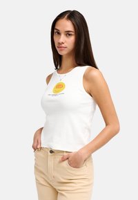 Débardeur en coton blanc avec encolure ronde et motif graphique jaune. Associé à un pantalon beige, montrant une coupe ajustée et un style décontracté.