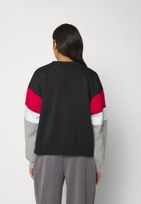 Sudadera negra con bloques de color rojo, blanco y gris, que presenta un escote redondo y mangas de gran tamaño. Textura suave, ajuste casual.