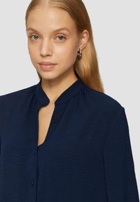 Marineblaue Bluse aus leichtem, strukturiertem Stoff. Mit Stehkragen und Knopfleiste. Lange Ärmel mit Gathered-Details.
