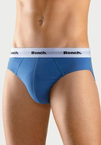 Blauwe slip van zacht materiaal, met een witte tailleband waarop het zwarte logo "Bench." staat. Het ontwerp is eenvoudig, aansluitend en glad van textuur.