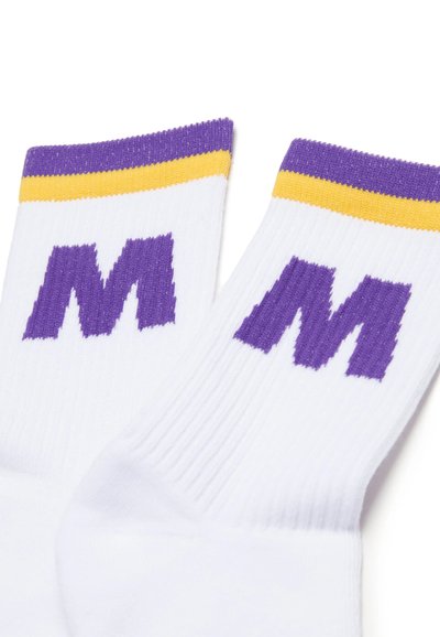 Calzini bianchi in cotone con texture a coste, caratterizzati da logo "M" viola e striscia gialla nella parte superiore. Il design sottolinea l'estetica sportiva.