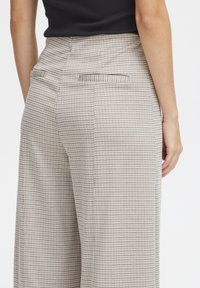 Beige Hosen mit kariertem Muster, ausgestattet mit Vordertaschen und einer glatten Textur. Die Taille ist angepasst und verjüngt sich zu weiten Beinen.