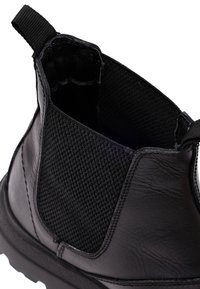 Botín negro con exterior de cuero elegante y forro de tela negra texturizada. Incluye una pestaña para facilitar el calzado. Suela de goma robusta.