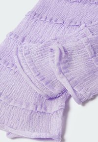 Tissu tricoté côtelé doux de couleur lilas avec des détails subtils de volants, plié sur une surface blanche.