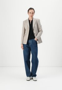 Světle šedý blazer se strukturovanými rameny, černý top pod ním, volné modré džíny a krémové boty. Jednoduchý, přizpůsobený design.