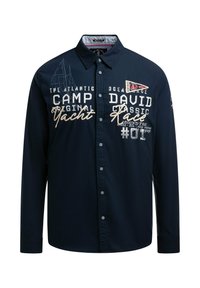 Marineblaue Langarmbluse mit Knopfverschluss, bestickt mit Text und Grafiken, darunter ein Segelboot-Design und kontrastierende Akzente.