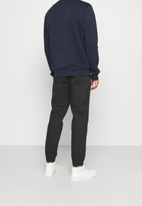 Marineblauwe sweatshirt met geribbelde manchetten en zoom, gecombineerd met zwarte, taps toelopende broek met elastische enkelboorden, gedragen met witte sneakers.