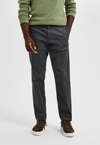 Grijze chinos met een slim-fit ontwerp, een gladde textuur en zijzakken. Gepaard met bruin suède veterschoenen en een groene trui.