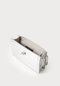 Malá obdélníková kovová stříbrná kabelka s řetízkem, s klopou a béžovým vnitřním podšívkou, otevřená na bílém pozadí.