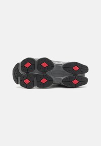 Svart sula på sneakers med en texturerad yta, prydd med röda diamantdetaljer på sulan. Anmärkningsvärda ruggade mönster för grepp.
