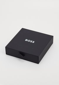Sort rektangulær boks med en glat overflade, der har ordet "BOSS" i hvidt på toppen og en lille træklaft til åbning.
