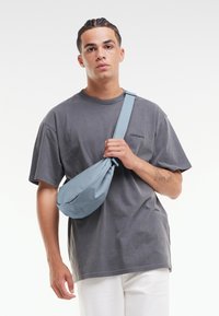 Grå oversized t-shirt, ljusblå axelväska med en mjuk textur, bärs över axeln. Slim fit vita byxor kompletterar looken.